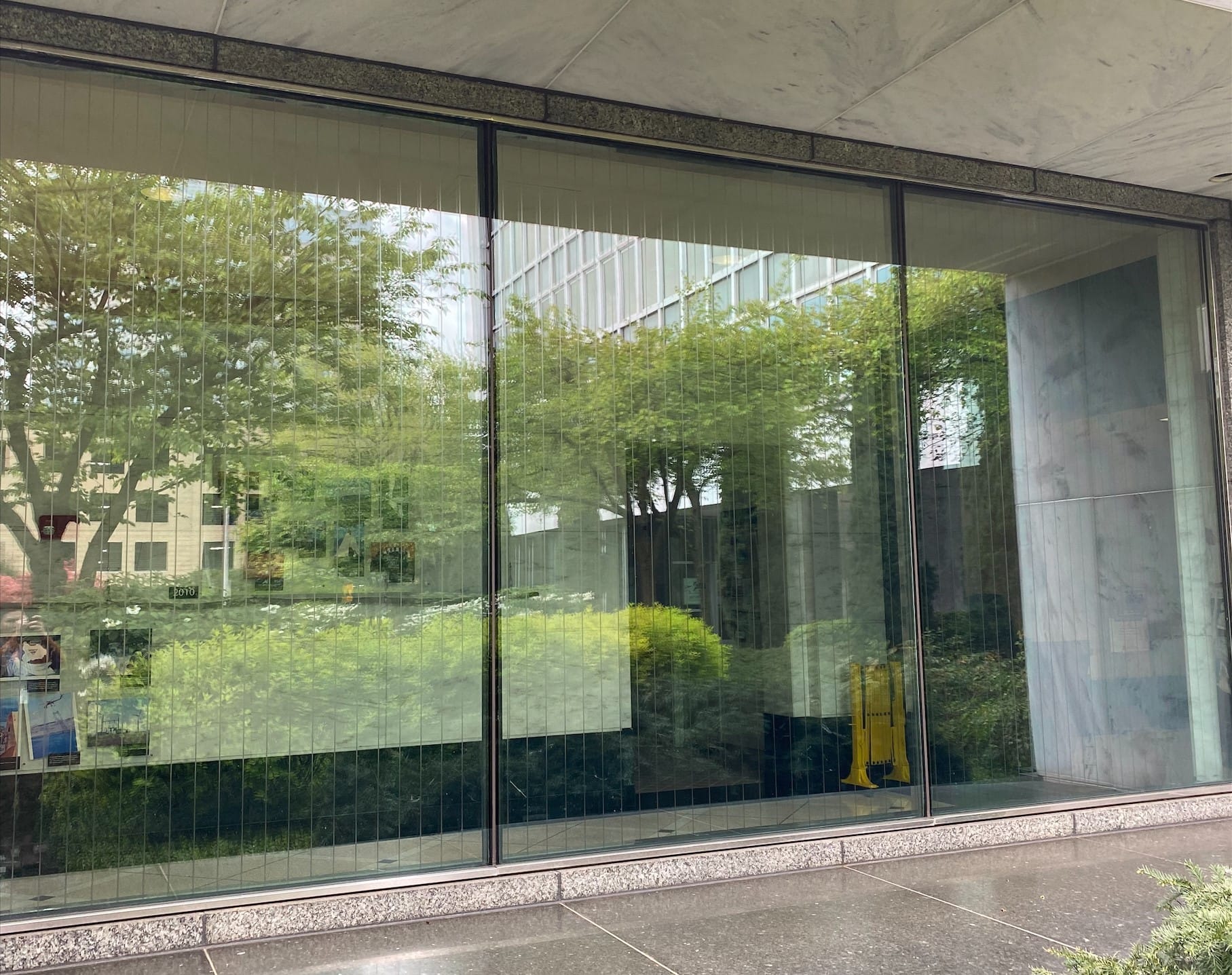 Großes Fenster mit Reflexionen der Außenwelt. Überklebt mit dünnen vertikalen Streifen zum Vogelschutz, welche kaum zu erkennen sind.